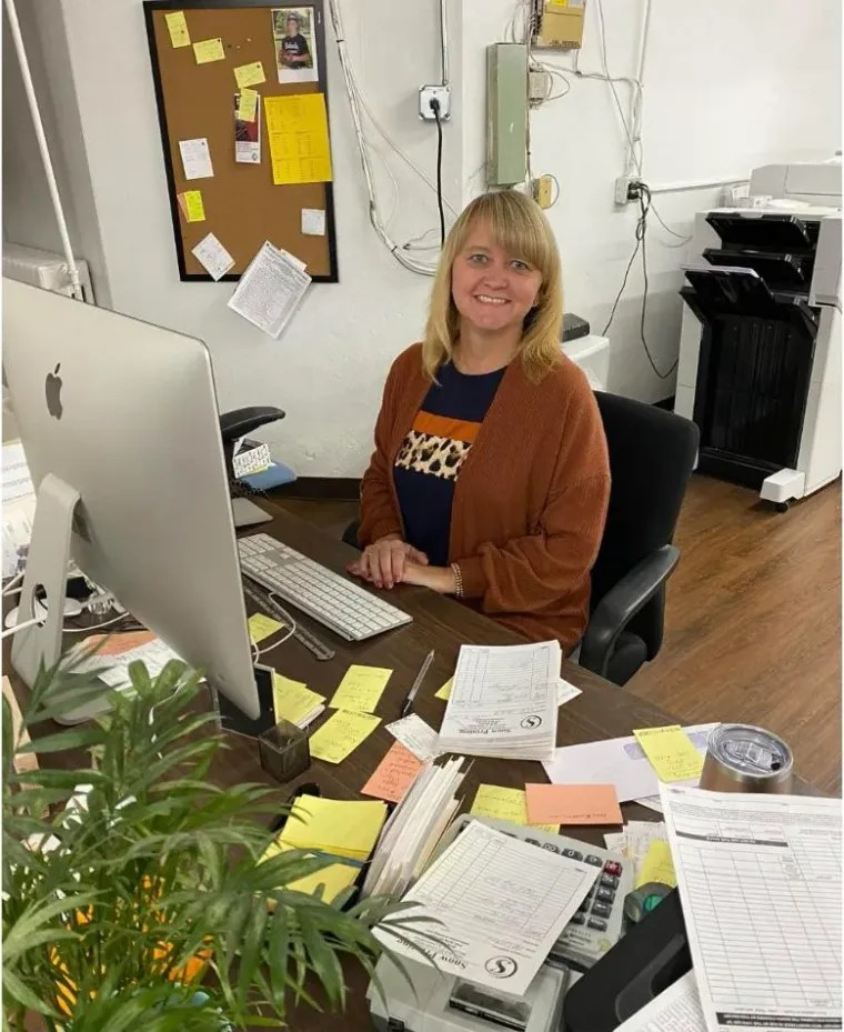 Melissa Sheeley smiling at the Snow Printing front desk, with job tickets beside her computer
