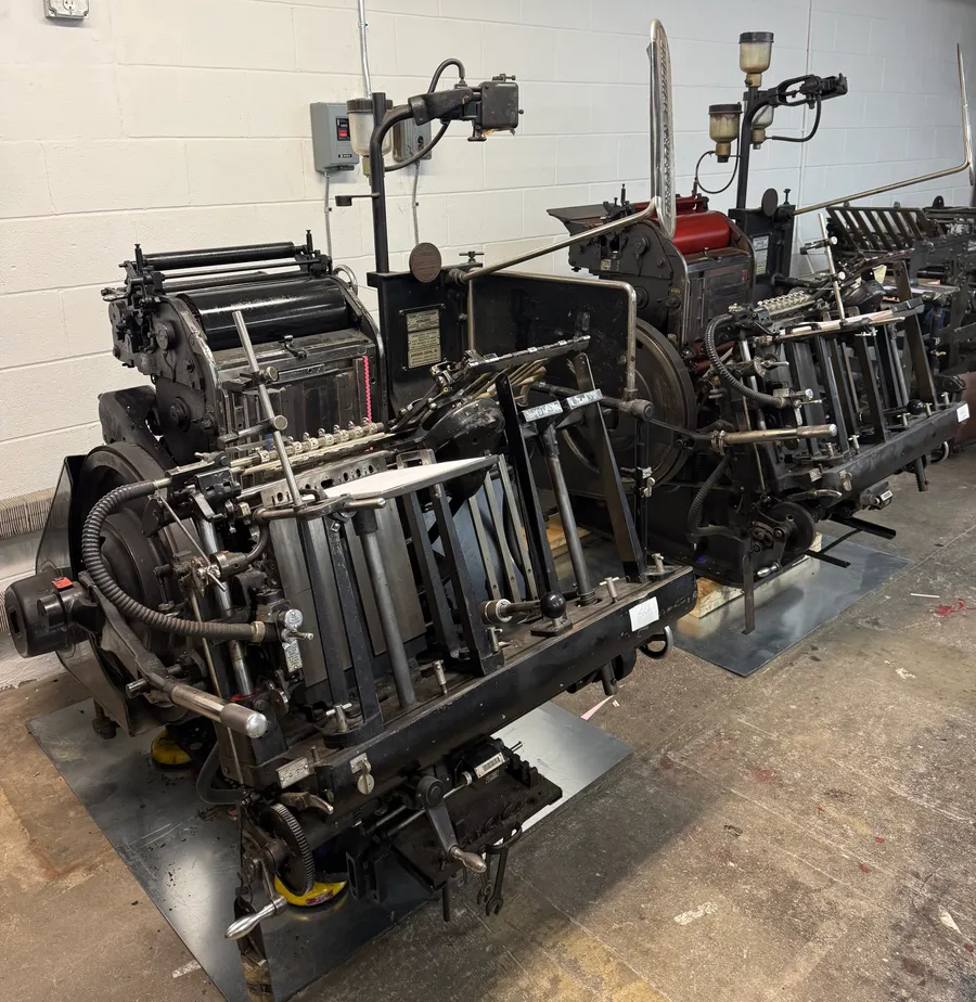 Two black Heidelberg platen presses side by side on the Snow Printing shop floor, one with red ink rollers